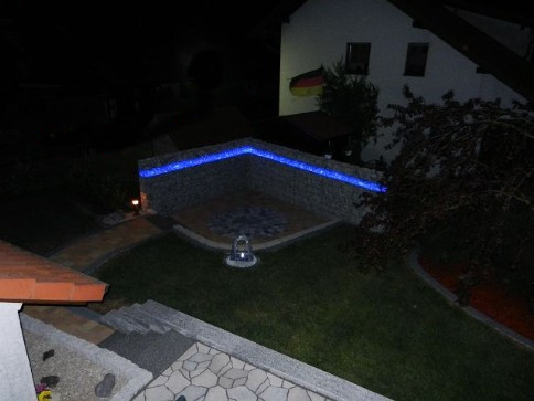Fertige Terrasse mit beleuchtetem Gabionenaufbau in der Farbe blau leuchtend