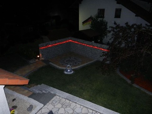 Fertige Terrasse mit beleuchtetem Gabionenaufbau in der Farbe rot leuchtend